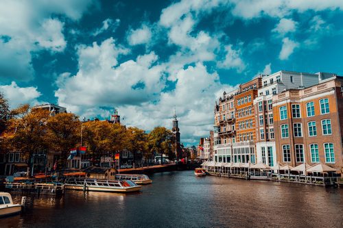 City view of Amsterdam with cruise boats and typical brick houses on sunny day with Vibrant fluffy clouds